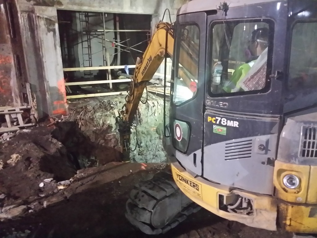 En kompakt elektrisk grävmaskin arbetar inomhus på en byggarbetsplats.